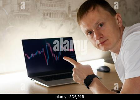 Primo piano della mano di un uomo che indica un grafico rosso a candeliera in declino sullo schermo di un notebook in un ufficio. Foto Stock