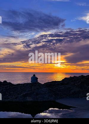 Cielo al tramonto sul mare e uomo solo seduto sulla riva Foto Stock