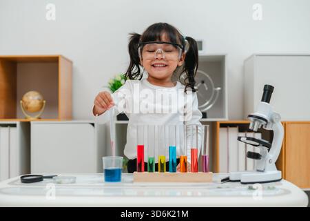 una ragazza felice, scienziata, studia utilizzando il liquido contagocce della pipetta con provetta e becher. imparare la scienza Foto Stock