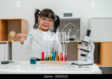 una ragazza felice, scienziata, studia utilizzando il liquido contagocce della pipetta con provetta e becher. imparare la scienza Foto Stock