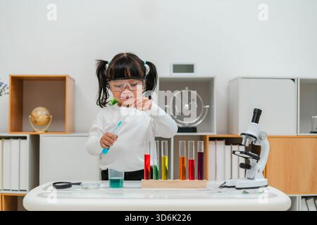 una ragazza felice, scienziata, studia utilizzando il liquido contagocce della pipetta con provetta e becher. imparare la scienza Foto Stock
