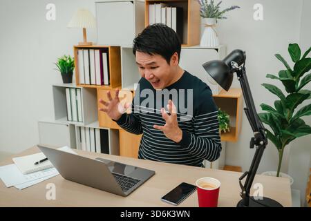 ha sorpreso il giovane uomo che lavora con un computer portatile a casa Foto Stock