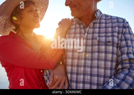 Sorridi, donna e cammina con l'uomo sulla spiaggia con amore, data di viaggio e legame in vacanza. Coppia felice, matura e abbracciata con affetto Foto Stock