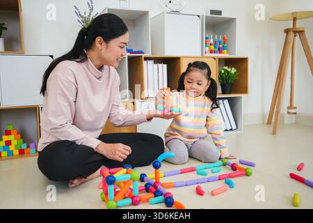 la bambina e la madre che giocano a casa giocano a un colorato giocattolo magnetico da costruzione Foto Stock