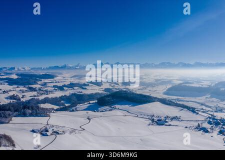 Panorama aereo invernale sulla campagna bernese innevata con le Alpi svizzere all'orizzonte Foto Stock