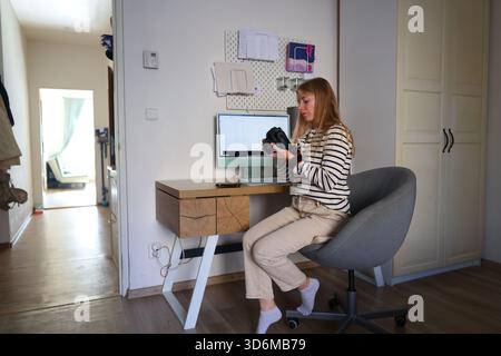 Giovane fotografa che tiene in mano una fotocamera DSLR e lavora in un accogliente e moderno studio. Foto Stock