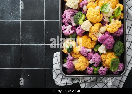 Cavolfiore colorato. Cavolfiore tagliato in piccoli pezzi in una teglia di ferro su un vecchio sfondo di mattonelle di pietra nera scura. Concetto di cucina alimentare e raccolto agricolo o background. Foto Stock