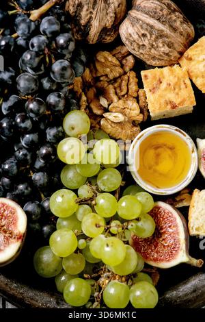 Antipasti di vino con diverse uve, fichi, noci, pane, miele e formaggio di capra su piatto di ceramica su vecchio sfondo di legno. Disposizione piatta, primo piano Foto Stock