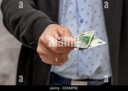 Un uomo con una camicia blu e un maglione tiene i soldi in mano, contando i soldi prima di spenderli. Foto Stock