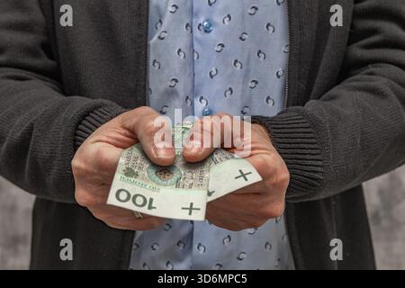 Un uomo con una camicia blu e un maglione tiene i soldi in mano, contando i soldi prima di spenderli. Foto Stock