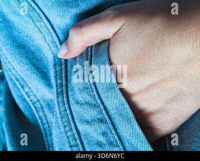 Primo piano di una mano appoggiata all'interno della tasca di una giacca in denim blu chiaro testurizzata o di un jeans Foto Stock