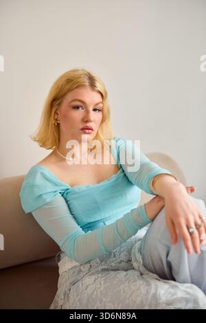 Giovane donna con top azzurro che si rilassa su un divano beige Foto Stock