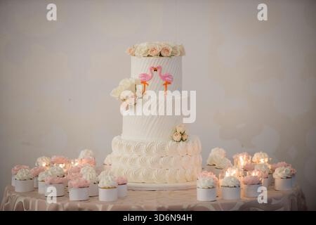 Torta nuziale a tre piani con Topper fenicottero rosa e Cupcakes Foto Stock