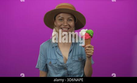 La donna tiene in studio un vivace cono gelato triplo con un ampio grin mentre presenta il dessert estivo: Gioia. Foto Stock