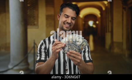 Il giovane ispanico in uniforme da arbitro ci tiene dei dollari sorridenti nelle strade della città vecchia durante il giorno. Foto Stock