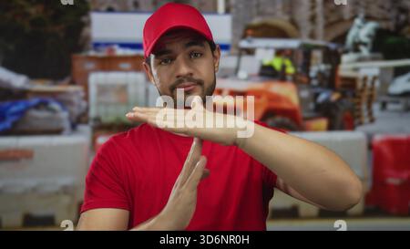 Uomo in camicia rossa fa un segnale di timeout con entrambe le mani all'interno dell'edificio in costruzione all'aperto alla luce del giorno; pausa. Foto Stock