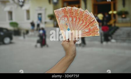 Uomo che detiene più banconote da 20 pesos filippine all'aperto in un ambiente urbano. Foto Stock
