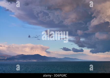 Spettacolari nuvole di tempesta sul mare calmo al tramonto dietro Mountain Horizon Foto Stock