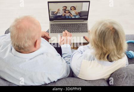 Una coppia senior seduto sul divano di casa e che sta videochiamando online con la famiglia utilizzando un laptop. Foto Stock