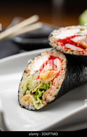 Sushi burrito a metà con nori, granchio, uova e verdure su piatto bianco con salsa di soia, primo piano Foto Stock