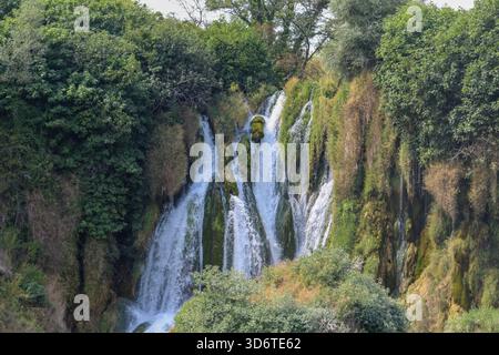 Una vista panoramica della cascata di Kravica in Erzegovina, caratterizzata da numerosi ruscelli a cascata che scorrono su scogliere rocciose e una fitta vegetazione verde. Foto Stock