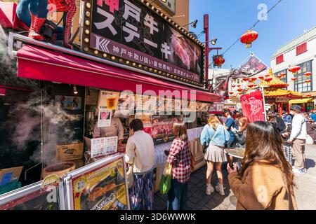 I turisti vengono serviti al famoso banco di cibo di manzo Kobe all'angolo di Nankinmachi Plaza. Sullo sfondo si trova il padiglione ottagonale cinese. Foto Stock