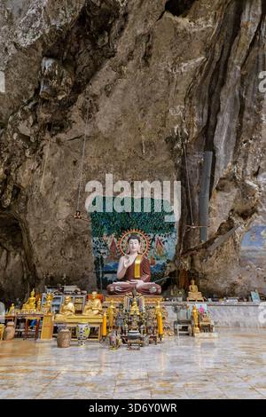 Grande statua di Buddha seduto circondata da piccoli Buddha dorati nella grotta di pietra calcarea presso il Tempio della Grotta della Tigre (Wat Tham Suea (sua)) a Krabi, Thailandia. Foto Stock