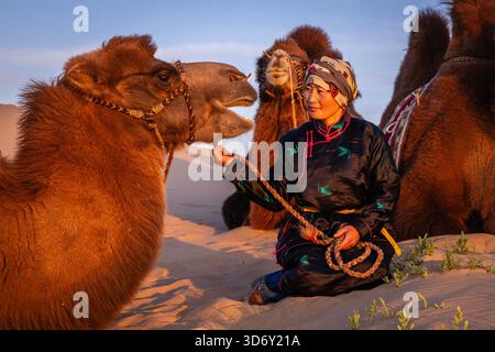 Ritratto di un allevatore di cammelli sul deserto del Gobi, sulle dune di sabbia di Khongor al tramonto, in Mongolia Foto Stock