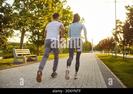 Vista posteriore di una coppia sportiva che fa jogging insieme nel parco al tramonto. Foto Stock