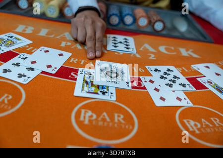 Mano del mazziere che spara carte su un tavolo di blackjack con chip e carte da gioco all'interno di un casinò, concetto di gioco d'azzardo, rischio, strategia, intrattenimento. Foto Stock