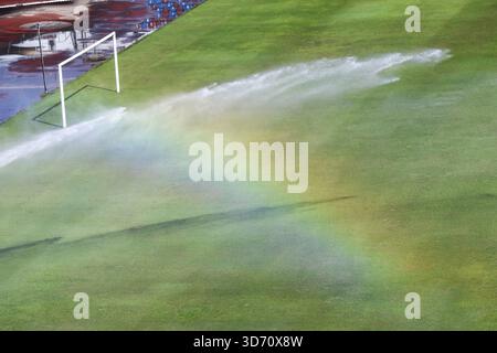 L'acqua rinfrescante dell'irrigatore crea un bellissimo arcobaleno sul campo da calcio in erba verde. Questo vibrante spettro di luce sul prato vicino a Goal crea speranze Foto Stock