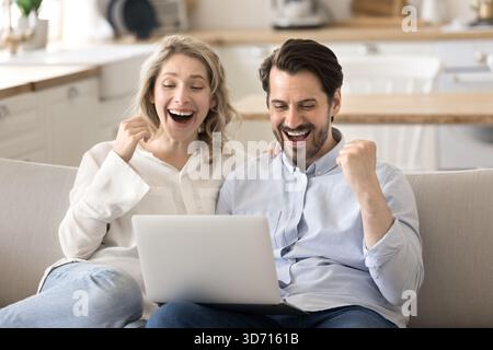 Felicissima coppia di famiglie sorprese alzano i pugni guardando lo schermo di un notebook Foto Stock