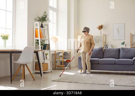 Legare la donna anziana disabile in abiti casual con la canna in piedi nel soggiorno di casa. Foto Stock