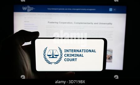 In questa immagine, una persona ha in mano un cellulare con il logo dell'organizzazione Tribunale penale internazionale (ICC) sullo schermo davanti alla pagina web. Foto Stock