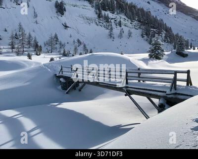 Paesaggio invernale idilliaco con un ponte di legno coperto di neve in luce soffusa e fredda vicino a Kandersteg nell'Oberland Bernese, Svizzera Foto Stock