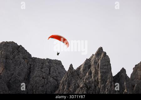 Un solitario parapendio si innalza vicino alle spettacolari scogliere calcaree della catena montuosa Wilder Kaiser in Tirol, Austria. La luminosa tettoia contrasta l'agai Foto Stock