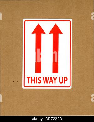 Etichetta in questa direzione, frecce rosse su sfondo bianco rivolte verso l'alto, su imballaggi in cartone di colore buff. Da questa parte, segno. REGNO UNITO Foto Stock