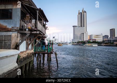 Contrapposizione tra sviluppo urbano e vita di classe a Bangkok, il fiume divide la città in due parti: Grattacieli con centri commerciali da un lato, povertà, baraccopoli e vecchie case informali sull'altra banca. Foto Stock
