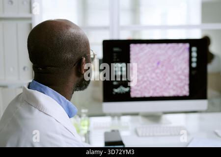 Uomo nero di mezza età che analizza l'immagine di un campione medico sul monitor del computer Foto Stock