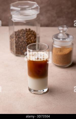 Caffè con latte di cocco e cubetti di ghiaccio in un bicchiere alto. Bevanda fredda analcolica tradizionale. Sullo sfondo, un vasetto di caffè e uno di zucchero. S Foto Stock