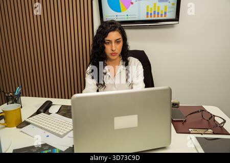 Giovane donna d'affari che lavora su un notebook, analizzando grafici e dati finanziari Foto Stock