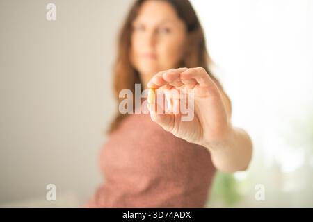 Donna incinta che esamina attentamente la pillola prima dell'assunzione mentre la tocca. Gestione accurata della salute durante il periodo di gestazione. Foto Stock