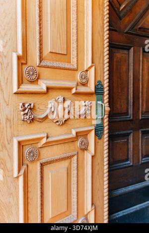 La porta in legno splendidamente lavorata presenta intagli dettagliati e una brillante maniglia in ottone che accoglie i visitatori con calore. Foto Stock