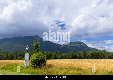 Religious statue overlooking a golden wheat field in Liptovske Matiasovce, Slovakia Foto Stock