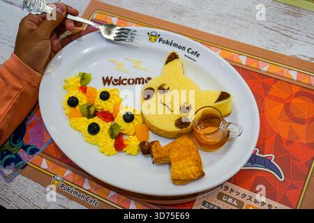 Il turista usa una forchetta per mangiare la voce del menu del Pokemon Cafe, Pikachu Souffle Pancake, con un messaggio di benvenuto a Nihonbashi, Tokyo, Giappone Foto Stock