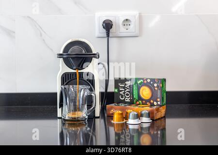 Primo piano della macchina Nespresso per preparare caffè con cialde Cafe Royal e tazza di vetro sul banco nero Foto Stock
