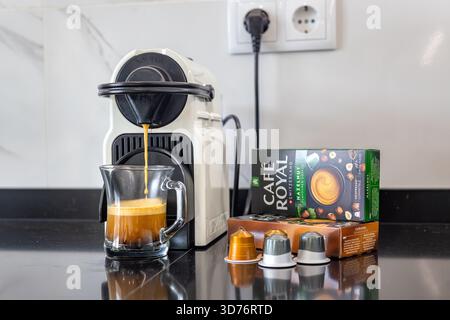 Primo piano del flusso di caffè con panna in tazza di vetro, macchina espresso e capsule box Foto Stock