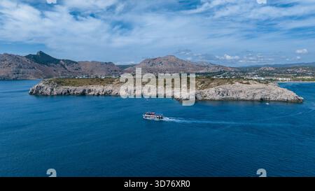 Vista aerea di una barca a vela sul mare blu profondo, con formazioni rocciose e montagne sullo sfondo, Kolympia, Rodos, Grecia. Foto Stock