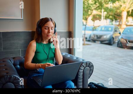Donna che lavora in telelavoro con un computer portatile e cuffie in un bar Foto Stock