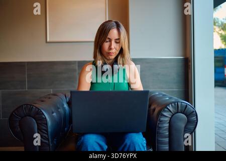Donna che lavora con un computer portatile in un bar con le cuffie Foto Stock